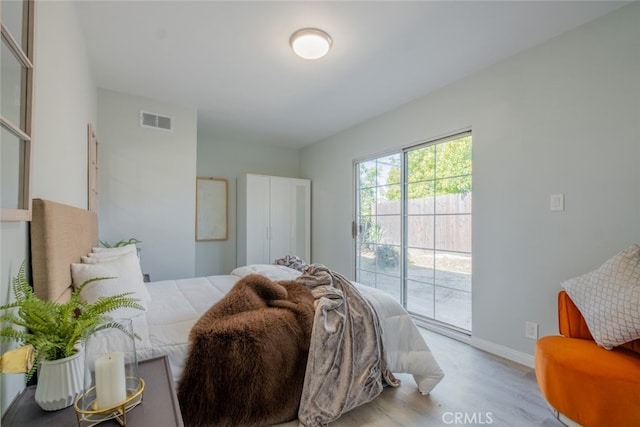 bedroom with baseboards, wood finished floors, visible vents, and access to exterior