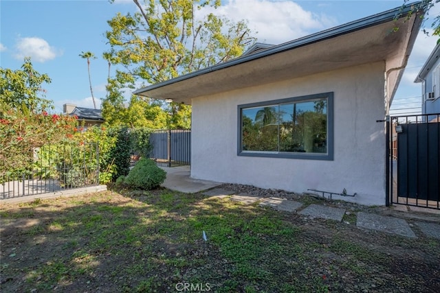 view of side of property with a gate, fence, and stucco siding