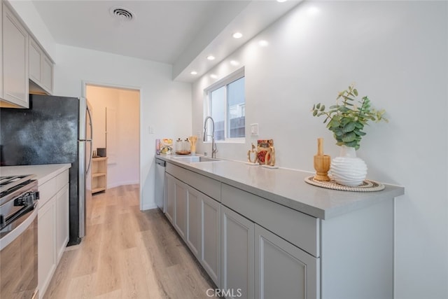 kitchen with visible vents, stainless steel appliances, light countertops, light wood-type flooring, and a sink