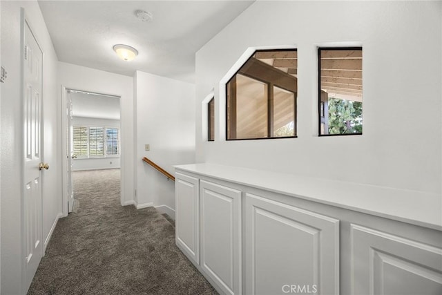 corridor with dark carpet, an upstairs landing, and baseboards