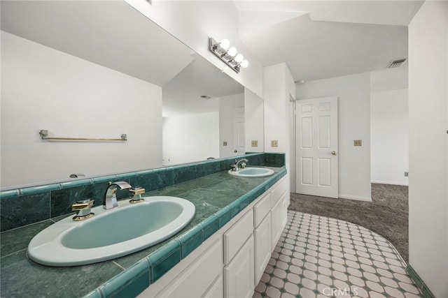 bathroom with double vanity, a sink, visible vents, and baseboards