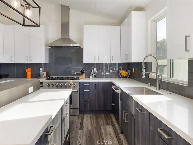 kitchen with decorative backsplash, lofted ceiling, light countertops, stainless steel stove, and wall chimney range hood