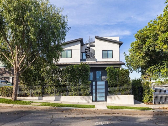 modern home with metal roof, a standing seam roof, fence, and stucco siding