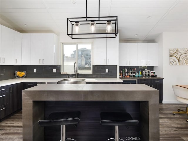 kitchen featuring decorative backsplash, a breakfast bar area, dark wood-style flooring, and a sink