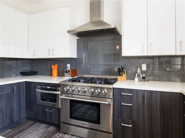 kitchen with wall chimney exhaust hood, appliances with stainless steel finishes, light countertops, and backsplash