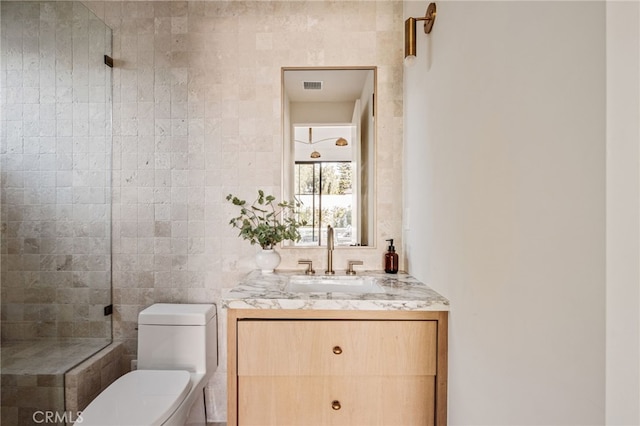 bathroom with visible vents, a shower, toilet, vanity, and tile walls