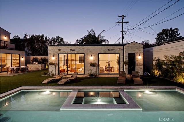 back of house with brick siding, a lawn, and a pool with connected hot tub