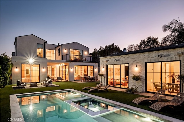 back of house at dusk featuring a fire pit, a patio area, french doors, a balcony, and a yard