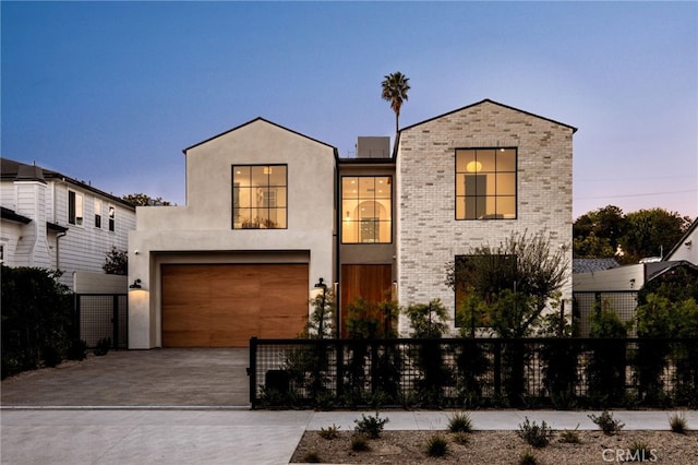 view of front facade with stucco siding, driveway, a fenced front yard, brick siding, and a garage