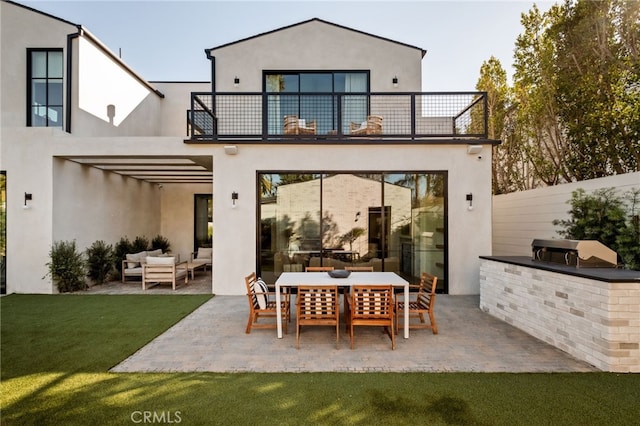back of property with stucco siding, outdoor lounge area, a balcony, exterior kitchen, and a patio