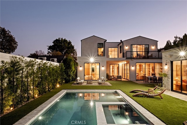 back of property with an outdoor hangout area, stucco siding, a balcony, an in ground hot tub, and a lawn