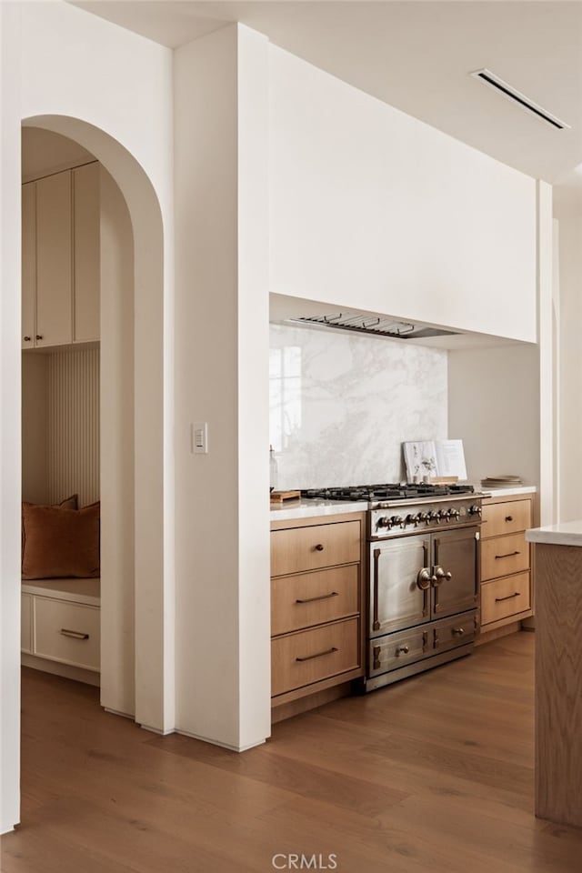 kitchen featuring light wood-style floors, range with gas stovetop, light brown cabinets, and tasteful backsplash