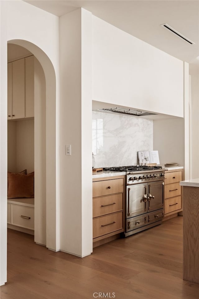 kitchen with gas range oven, tasteful backsplash, light brown cabinetry, and light wood finished floors