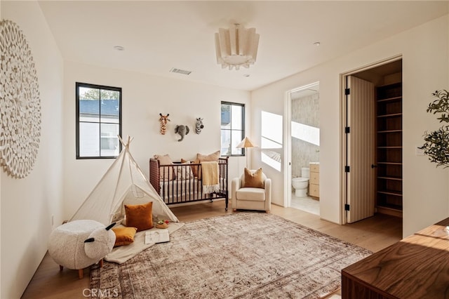 bedroom featuring ensuite bath, visible vents, and wood finished floors