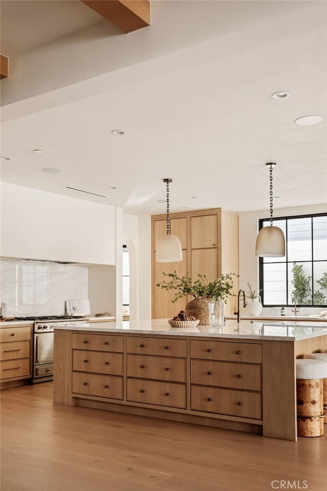 kitchen with light countertops, light brown cabinetry, decorative backsplash, pendant lighting, and light wood-style flooring