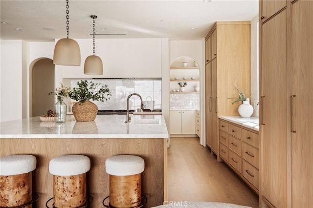 kitchen with light brown cabinetry, light wood finished floors, a sink, and a breakfast bar