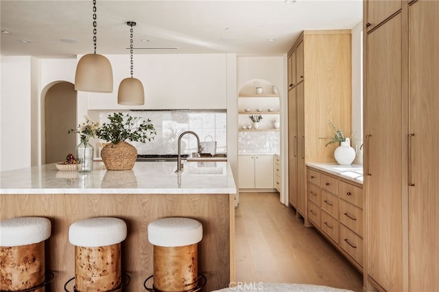 kitchen with light brown cabinetry, light wood-style floors, a kitchen breakfast bar, and a sink