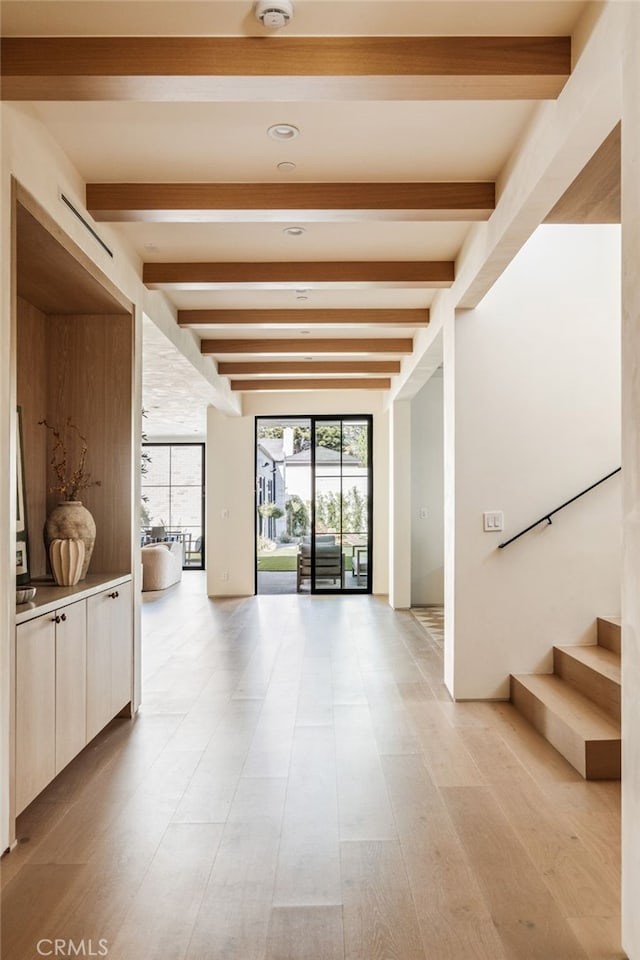interior space featuring light wood finished floors, beam ceiling, and stairway
