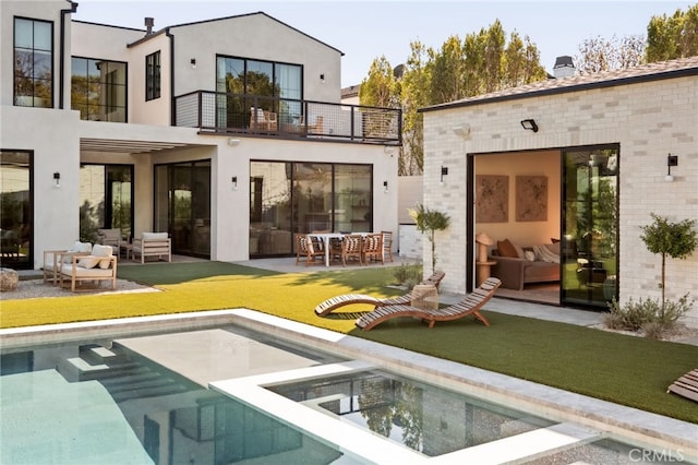 rear view of house with an outdoor pool, a balcony, an outdoor hangout area, a patio area, and stucco siding