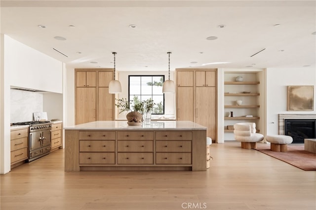 kitchen featuring high end stainless steel range, light brown cabinetry, a glass covered fireplace, a kitchen island, and light wood-type flooring