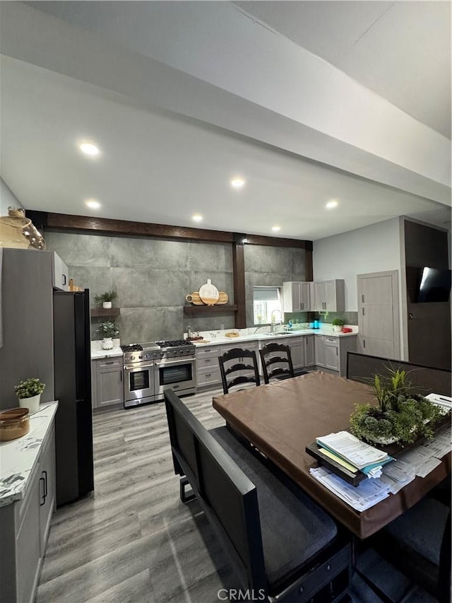 kitchen with freestanding refrigerator, light countertops, gray cabinetry, double oven range, and a sink