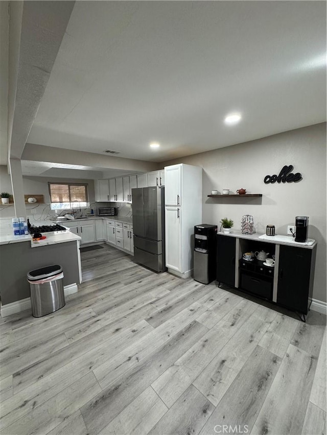 kitchen featuring stainless steel appliances, light wood finished floors, open shelves, and light countertops