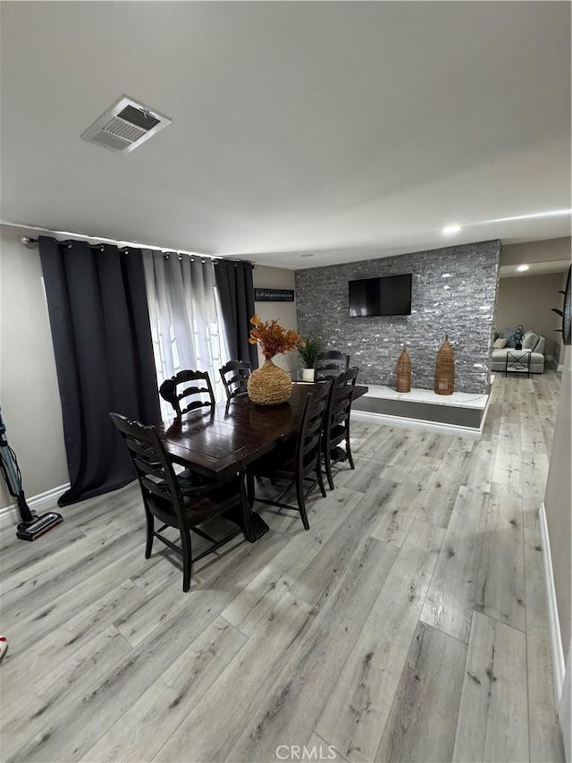 dining area with light wood-type flooring, visible vents, and baseboards