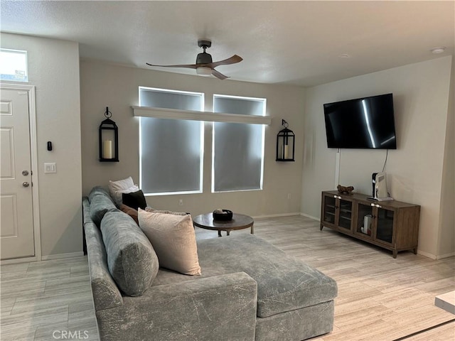 living room with a ceiling fan, baseboards, and light wood finished floors