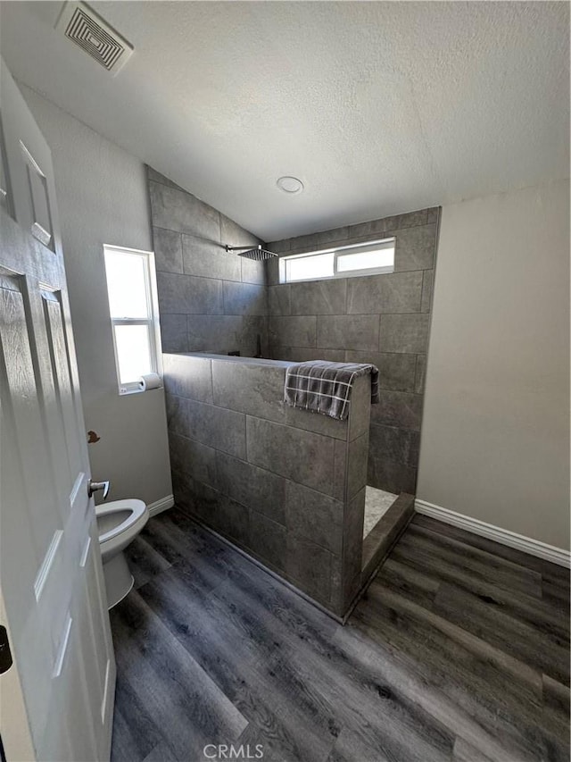 full bathroom featuring a walk in shower, a textured ceiling, toilet, wood finished floors, and visible vents