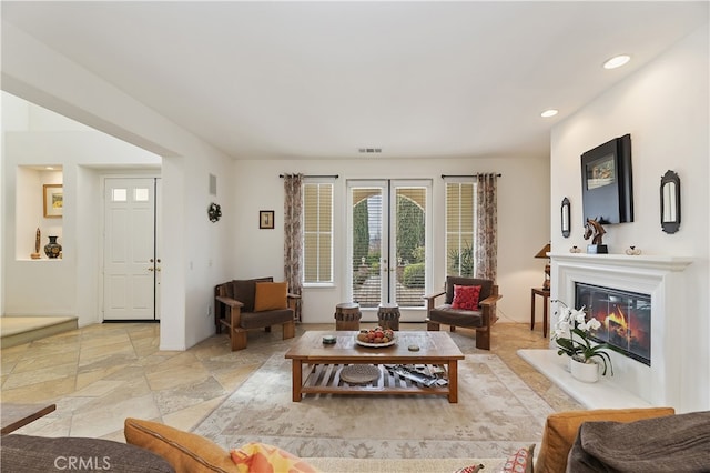 living room with visible vents, recessed lighting, stone tile flooring, french doors, and a glass covered fireplace