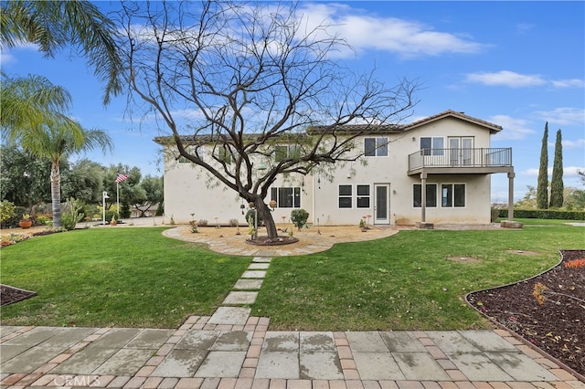 rear view of property with a balcony, a lawn, and stucco siding