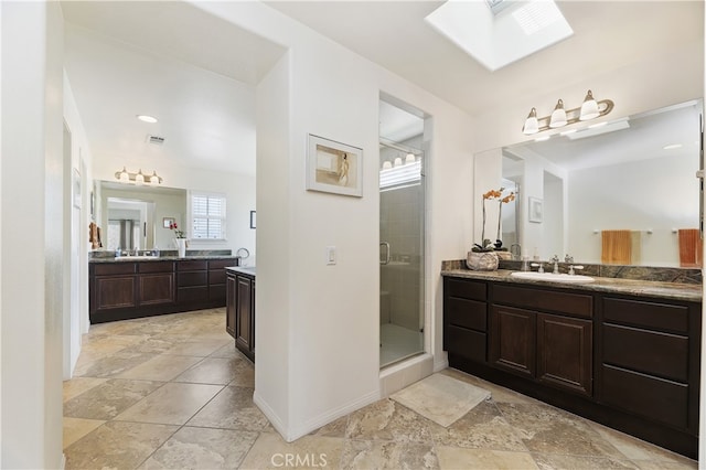 bathroom featuring a stall shower, a skylight, two vanities, and a sink