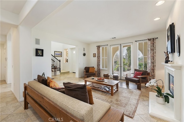 living area featuring recessed lighting, visible vents, a glass covered fireplace, and stairs