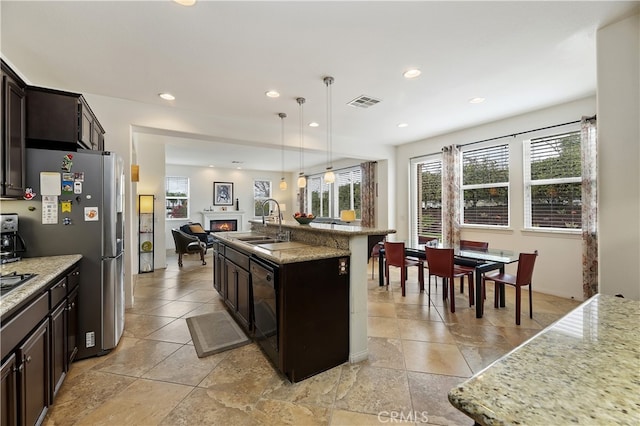 kitchen with visible vents, a sink, open floor plan, a lit fireplace, and dishwasher