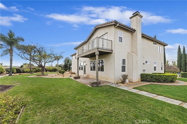 rear view of property featuring a yard, a patio, a chimney, and a balcony