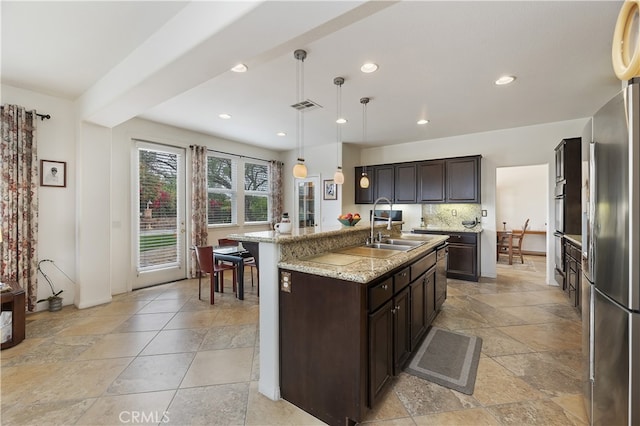 kitchen featuring visible vents, backsplash, dark brown cabinetry, freestanding refrigerator, and a sink