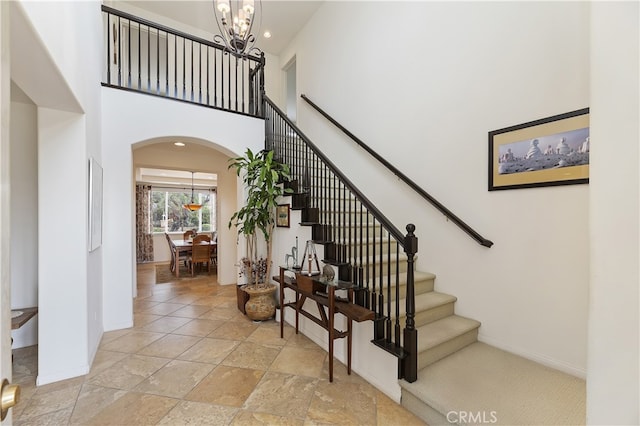 staircase with a notable chandelier, stone finish floor, arched walkways, a high ceiling, and baseboards