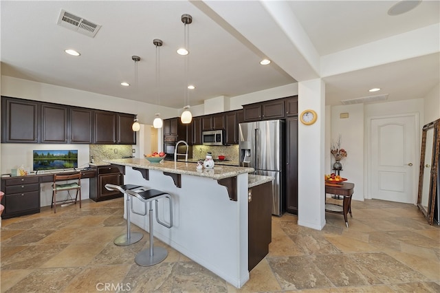 kitchen featuring visible vents, a kitchen breakfast bar, stone tile floors, dark brown cabinetry, and appliances with stainless steel finishes