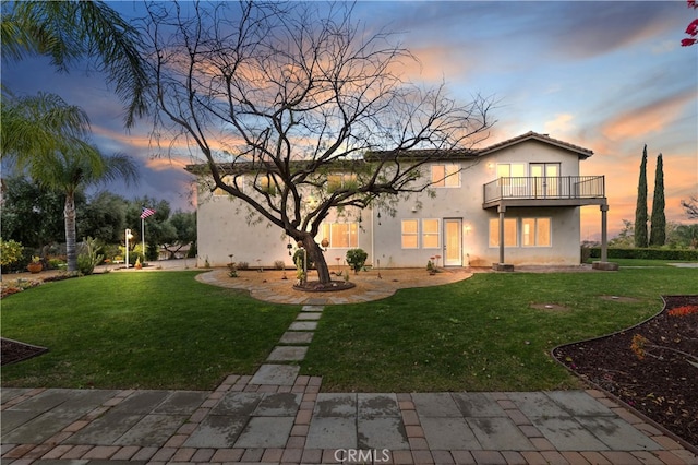 back of house with stucco siding, a lawn, and a balcony