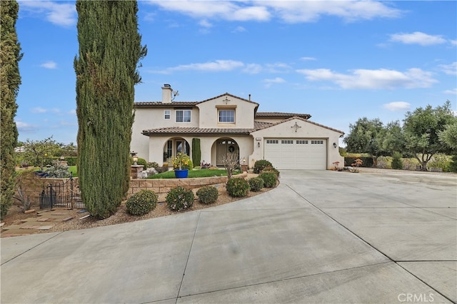 mediterranean / spanish house with driveway, a chimney, stucco siding, a garage, and a tiled roof