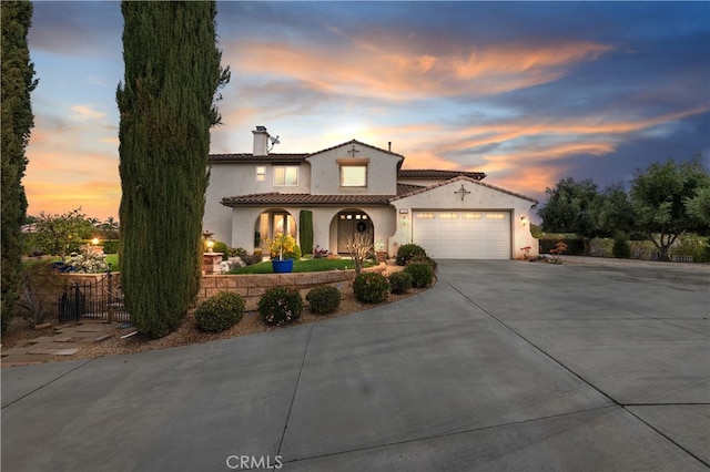 mediterranean / spanish home featuring stucco siding, driveway, fence, an attached garage, and a chimney