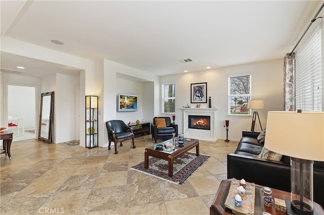 living room featuring visible vents, recessed lighting, stone finish floor, and a glass covered fireplace