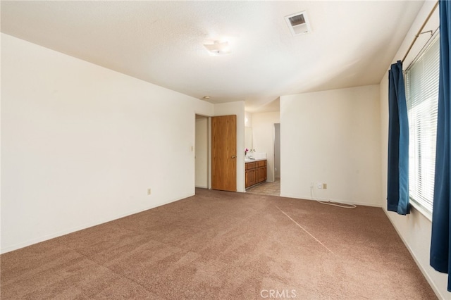 unfurnished bedroom featuring light colored carpet, visible vents, and ensuite bathroom