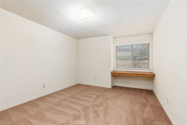 carpeted spare room featuring baseboards and built in study area