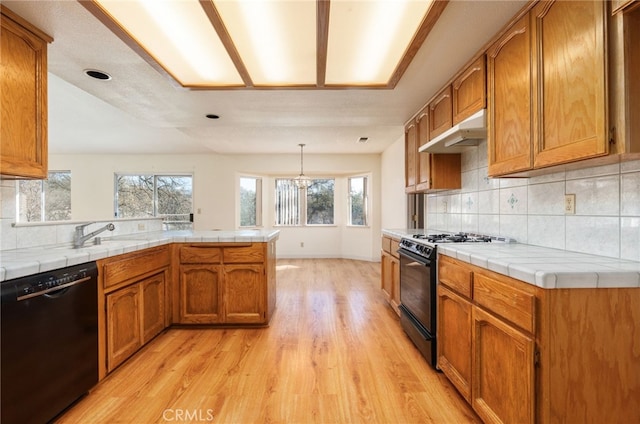 kitchen featuring tile countertops, black appliances, a peninsula, and under cabinet range hood