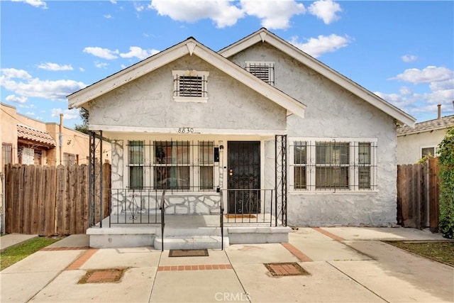 bungalow-style house featuring a porch, fence, and stucco siding