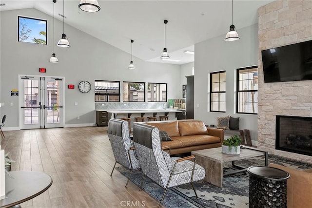 living area with high vaulted ceiling, a stone fireplace, light wood-style flooring, and a healthy amount of sunlight