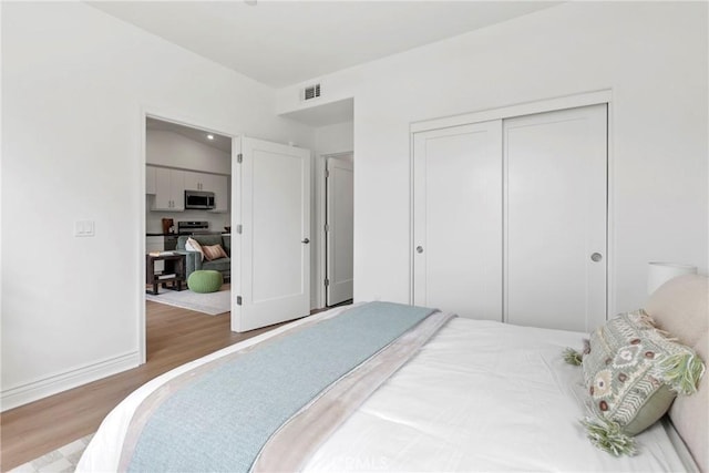 bedroom with wood finished floors, visible vents, a closet, and baseboards