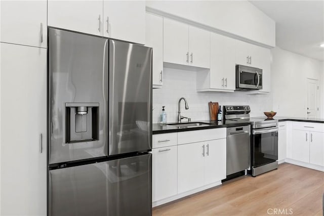 kitchen with dark countertops, decorative backsplash, light wood-style flooring, stainless steel appliances, and a sink