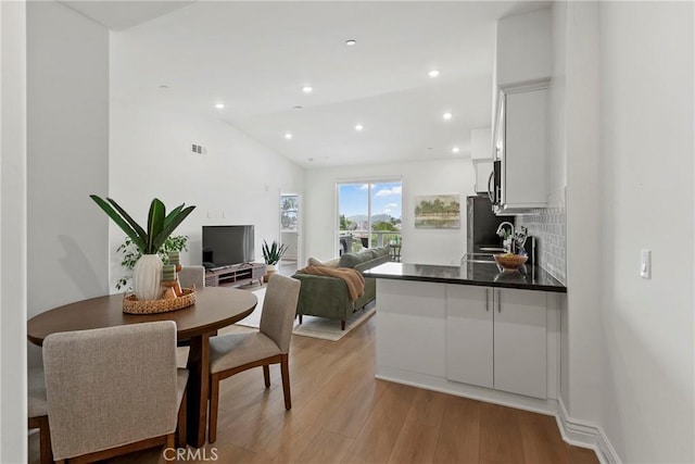 kitchen with light wood-style flooring, a sink, white cabinets, decorative backsplash, and vaulted ceiling